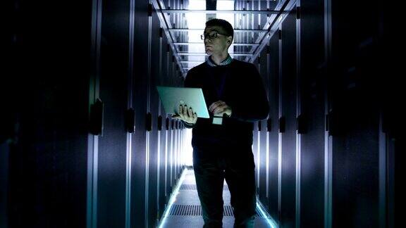 男性服务器工程师带着打开的笔记本走过一排排机架服务器他在大型未来数据中心工作