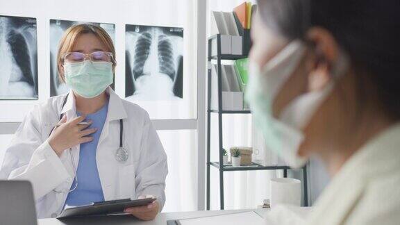 年轻的亚洲女医生戴着防护口罩使用笔记本电脑正在医院办公室与女病人谈论结果或症状