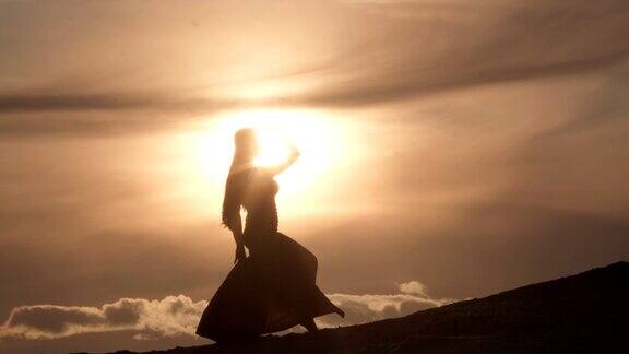 日落时分美丽的年轻女子在沙丘上跳着中东舞轮廓