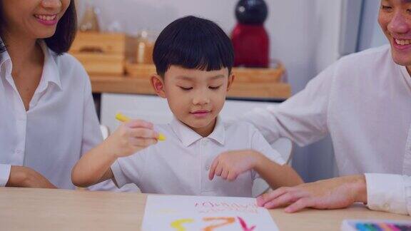 可爱的亚洲小儿子在家里和父母一起在纸上画画快乐的家庭活动小男孩小朋友在客厅和爸爸妈妈一起学习画画享受创意