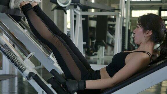 年轻有魅力的亚洲女人在健身房训练腿运动女子训练她的四头肌在机器压在健身房慢动作保健、健身和健美