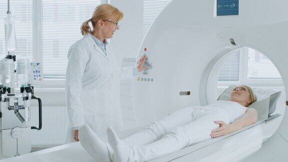 在医学实验室放射学家控制MRI或CT或PET扫描与女性病人正在进行的程序高科技现代医疗设备友好的医生与病人聊天