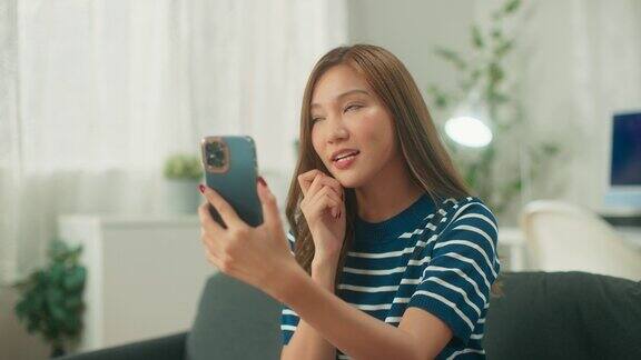 亚洲女性拿着智能手机在现代房间里和朋友视频通话快乐的内容创作者在家用社交媒体应用程序视频自拍