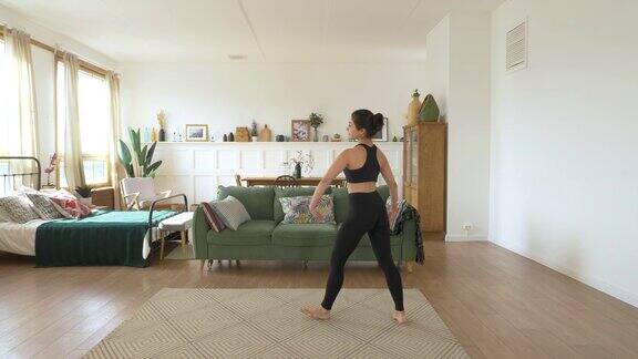 一个年轻的印度女芭蕾舞演员在家里训练在明亮舒适的房间里做动感运动穿着黑色上衣和打底裤运动理念健康生活