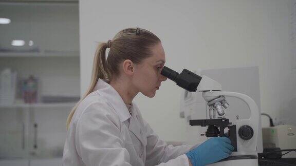 在实验室工作时使用显微镜的女科学家现代医学研究实验室女实验室助理看着显微镜分析样本生化物质验血