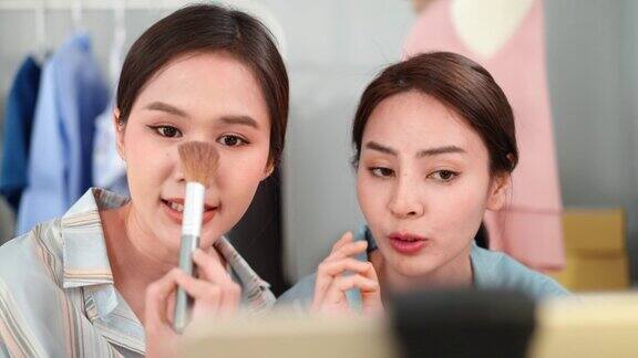 两位年轻貌美的亚洲博主利用智能手机摄像头在社交网络上直播视频建议用刷妆的粉底来打造自然妆容在线销售