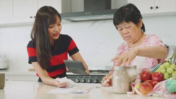年轻的亚洲妇女和她的母亲在厨房里整理支付账单和家庭财务通货膨胀高生活成本