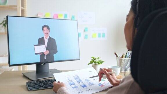 年轻的ui设计开发人员程序员手持平板电脑屏幕上显示着移动应用程序原型同时与团队在家中办公进行虚拟视频会议