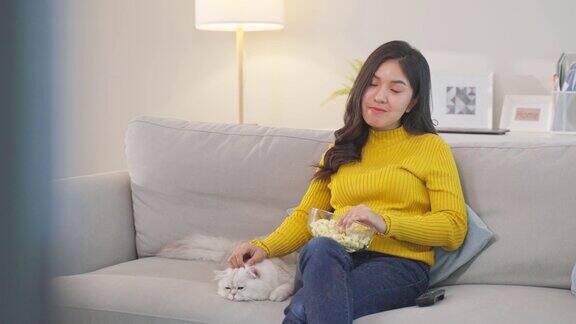 亚洲美丽的女人抚摸家可爱的猫看电影有魅力的年轻女性坐在沙发上与她的小宠物猫与温柔的闲暇时间在家里的客厅