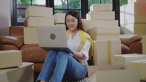 一名年轻的亚洲女性正在使用笔记本电脑与消费者交流在她家的客厅里在线销售产品