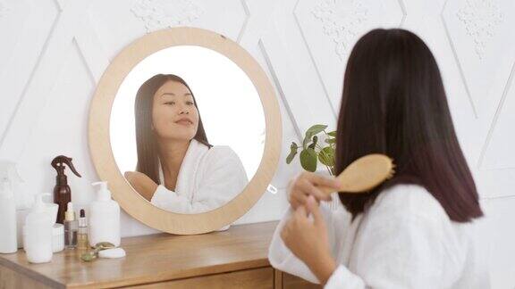 每天都美丽年轻迷人的和平亚洲女士梳理她的头发与刷子看着镜子在卧室