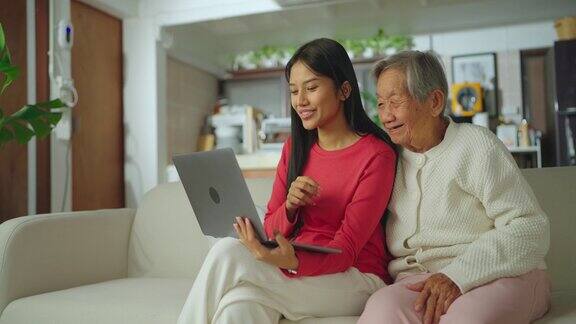 年轻的亚洲女人和她的祖母在客厅使用笔记本电脑