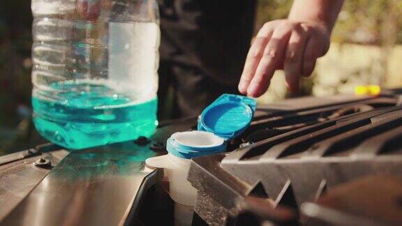 一名男子打开挡风玻璃清洗液储液器的盖子倒入蓝色防冻液用于清洗玻璃慢镜头特写