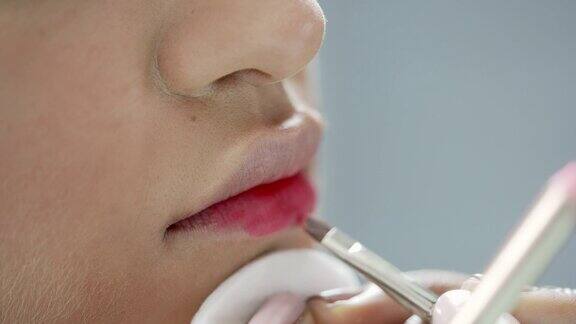 一名化妆师用唇刷小心翼翼地将口红涂抹在模特的嘴唇上