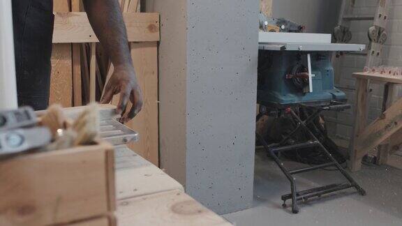 一个非洲裔美国人把木板放进木工机器然后拿锯末