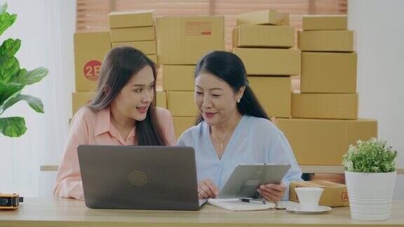 一名亚洲妇女和她的母亲在家用笔记本电脑和平板电脑在网上销售中小企业