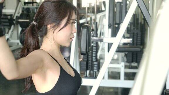年轻的运动亚洲女人在健身中心的重量机器上锻炼缓慢的运动运动和运动概念
