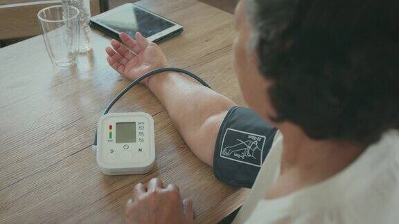 一位老年妇女正在家中用数字压力表测量自己的血压和心率