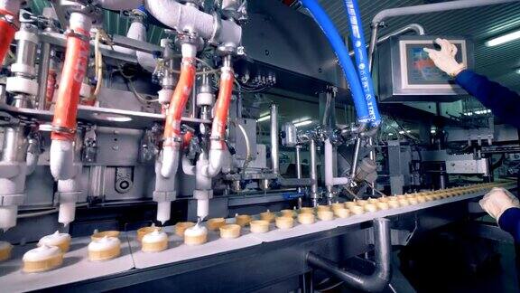 工业机器正在往晶圆杯里装白色冰淇淋而工厂工人正在设定参数