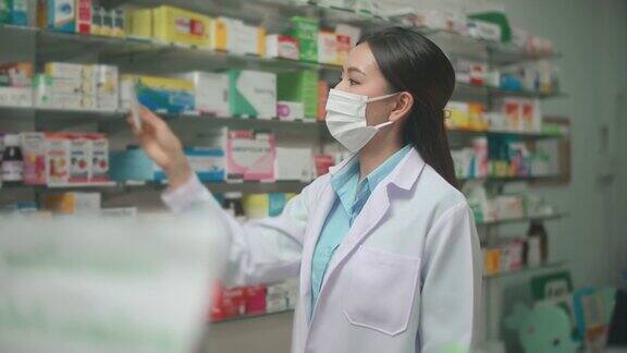 一名亚洲女药剂师戴着防护面具和实验服在现代药店为顾客选择药物