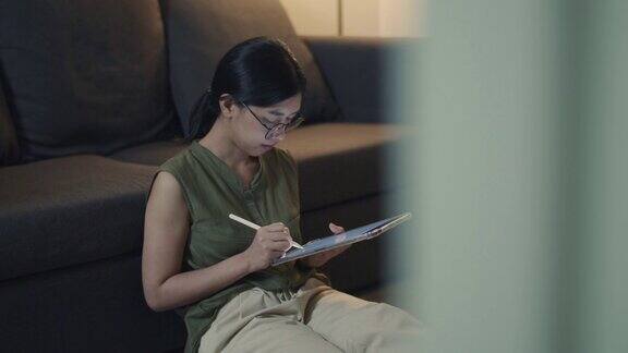 亚洲女性晚上坐在客厅的沙发上用数码平板电脑看新闻