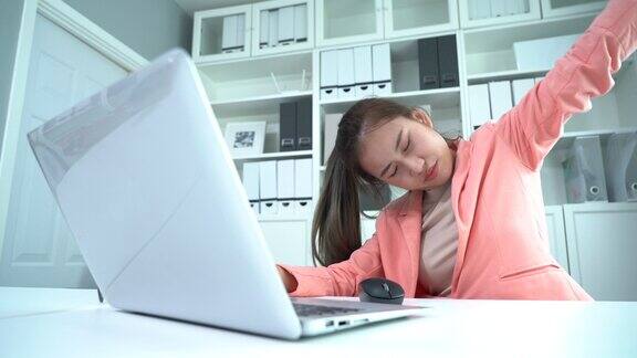 亚洲年轻女商人使用笔记本电脑患有颈部疼痛和伸展手臂在工作场所办公室综合症在书桌上伸伸懒腰放松一下久坐过度工作