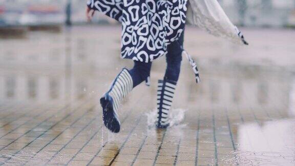 大雨过后穿着胶靴的女孩在水坑里奔跑跳跃在雨后玩耍的女人慢动作