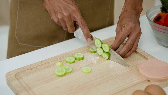 特写亚洲男子用菜刀将小黄瓜切成圆形准备晚上做饭时自己吃假期不要离开家手指糊上石膏