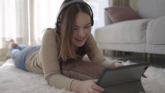 年轻的亚洲妇女在家里休息的时候用平板电脑听音乐