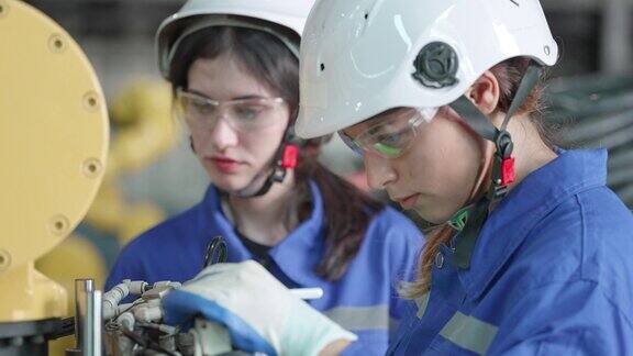 多种族女性工业专家穿着安全制服在机器人手臂工厂从事自动化生产在机器人仓库安装机器人手臂程序后检查文件项目或在制造工厂测试操作