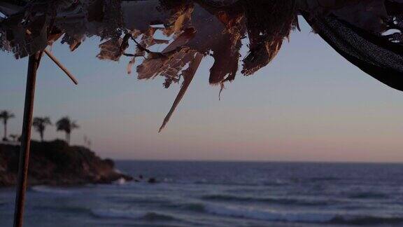 破碎的纺织品在微风中挂在废弃的亭子屋顶上背景是湛蓝的地中海海浪日落时分塞浦路斯的海湾没有人