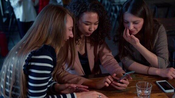 社交媒体三个年轻美丽、快乐的多民族女性朋友在咖啡馆一起使用智能手机