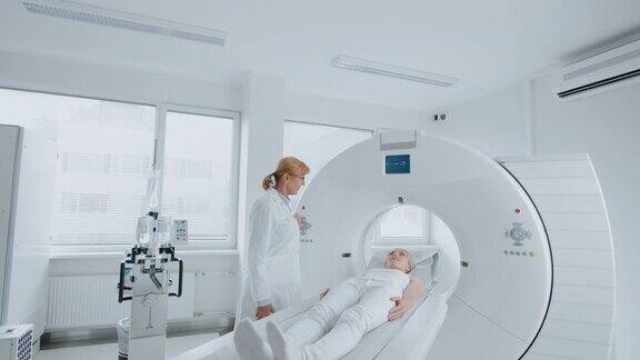 在医学实验室女性放射学家控制MRI或CT扫描与女性病人进行程序高科技现代医疗设备