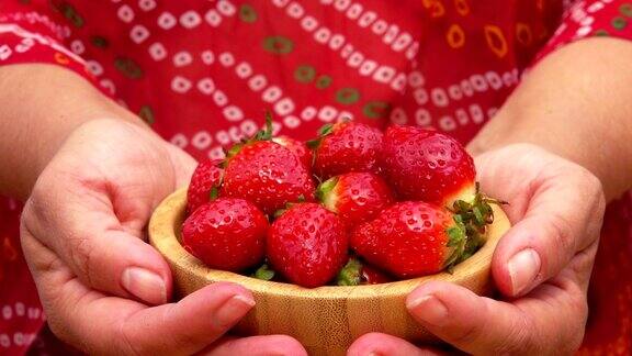 女人的手正拿着一个盛着鲜红多汁草莓的碗