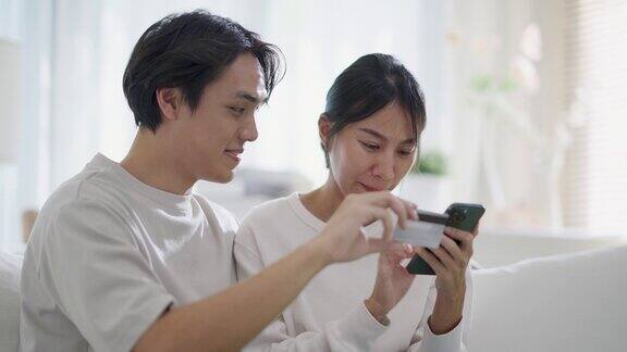 年轻夫妇坐在家里舒适的沙发上通过智能手机上网购物