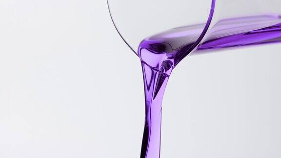 紫色的油正从烧杯倒在灰色的背景