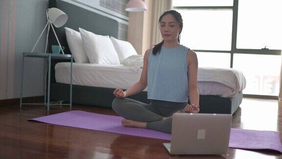 亚裔中国女性在家庭卧室里用笔记本电脑进行在线课程练习瑜伽