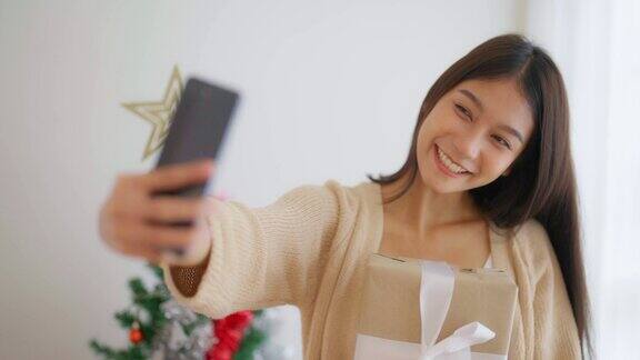 年轻的亚洲妇女正在与她的朋友进行轻松愉快的自拍和视频通话女性在与朋友视频对话时展示礼品盒新年快乐感恩节快乐