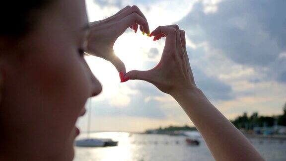 手做成心形在夏天的日落海上美丽的女人做爱的象征