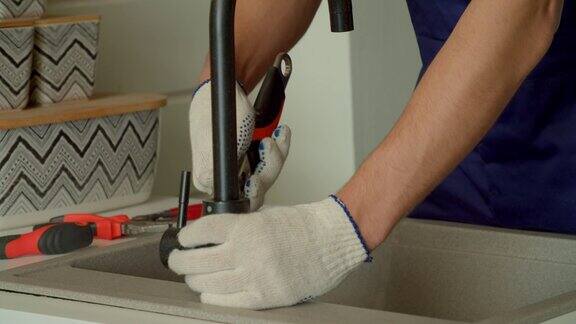 戴着防护手套的男性用工具修理厨房水龙头的特写