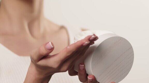 一个女人从一个罐子里拿起奶油保湿乳液在她的手上涂抹保湿霜的特写