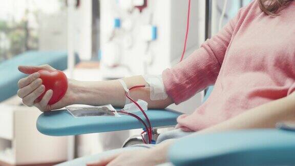 女性献血者的手的特写镜头白人妇女挤压心形红球将血液通过管道泵入袋中为意外事故受害者捐款