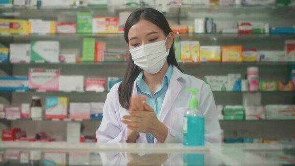 亚洲女性药剂师戴着医用外科口罩使用酒精凝胶在现代药店的肖像covid-19和大流行概念