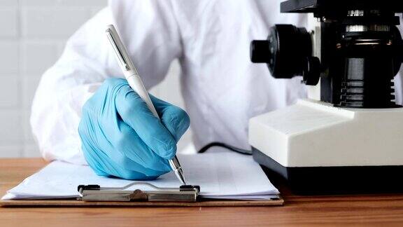 医学保健生物学病毒检测药物治疗试验试验室配有医学专家穿着白色防护服俯视显微镜