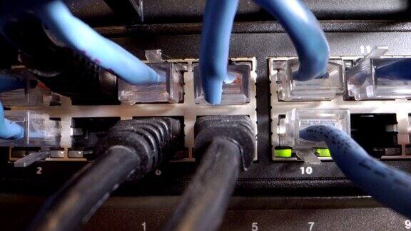 在IT组网柜背景中Cat5e以太网线缆插入交错的、杂乱的高速千兆因特网Cat5数据补丁线缆闪烁的网络交换机