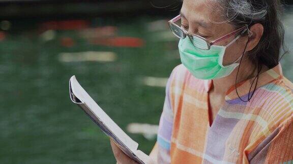 戴着外科口罩和眼镜的老年妇女喜欢在户外看书