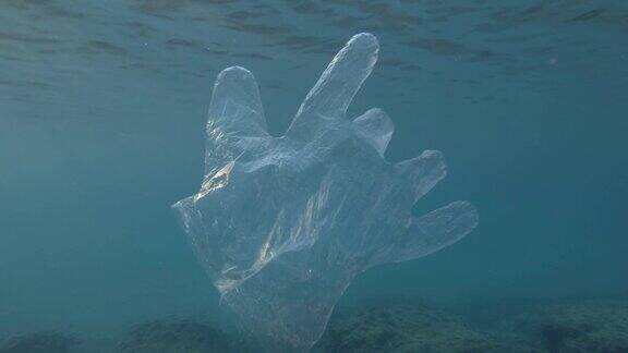 塑料污染废弃的塑料手套在阳光下慢慢漂浮在蓝色的水面下透明塑料手套漂浮在欧洲地中海慢动作