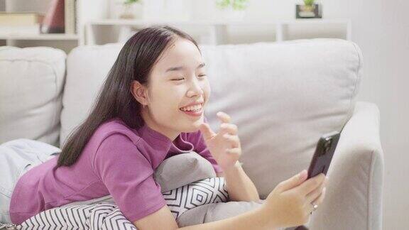 一个单身的亚洲女人的生活方式愉快地放松和聊天的朋友在家里的客厅用手机