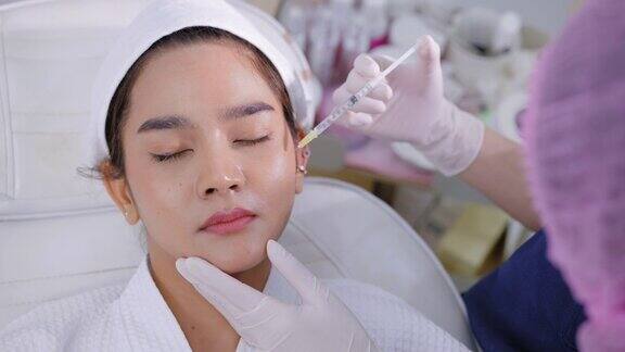 女病人脸上带着幸福的微笑医生戴着卫生手套、发帽为正在注射肉毒杆菌的年轻亚洲妇女提供医疗服务穿着浴衣在眼部注射维生素C躺在白色的医疗沙发上