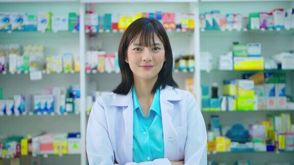 年轻的亚洲女药剂师在药房柜台微笑着拿着药品对着镜头